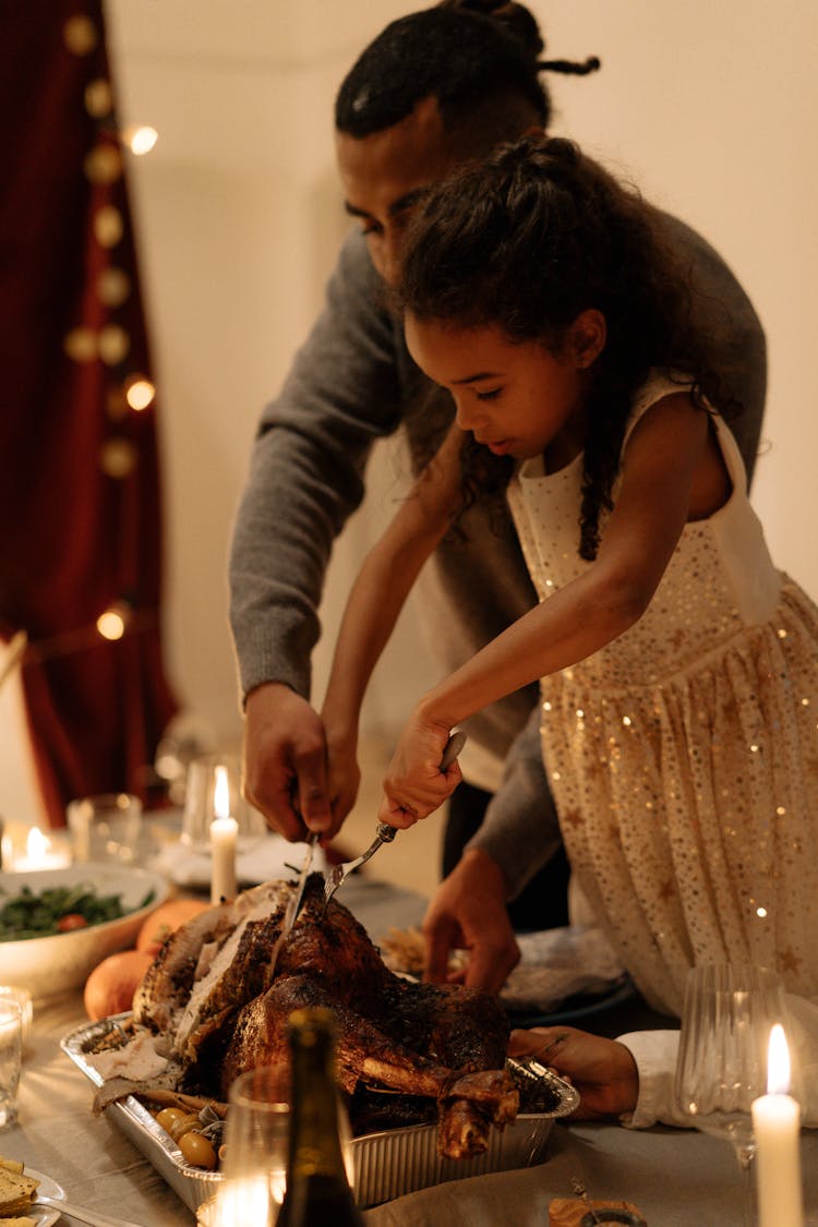 Man In Gray Long Sleeve Shirt Helping His Daughter Slicing The Turkey