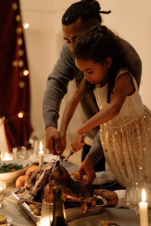 Free A father and daughter sharing a festive moment carving a turkey together at a holiday meal. Stock Photo