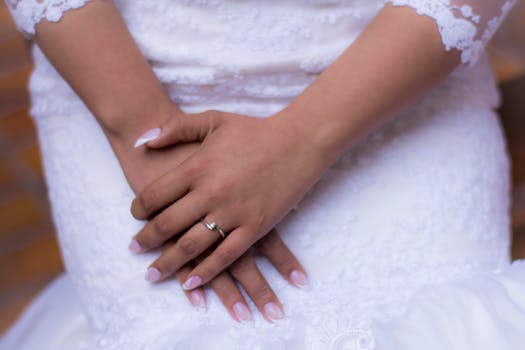 Close-up of a bride's hands wearing a silver ring, resting on a white lace wedding dress.