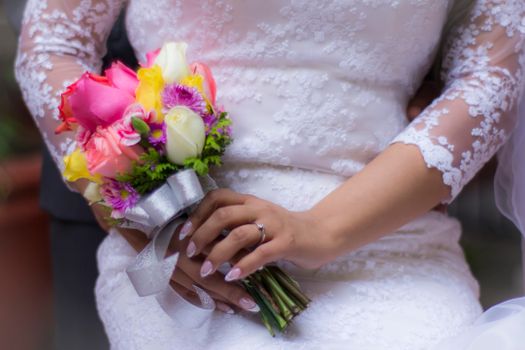 A close-up of a bride in a lace dress holding a vibrant wedding bouquet.