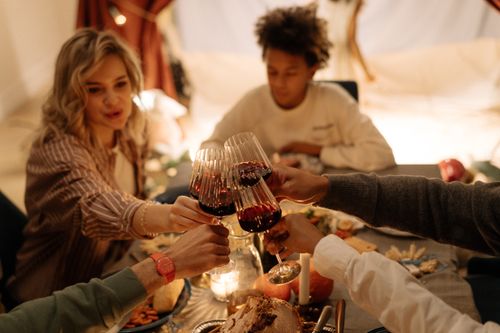 Free A group of friends toasting with red wine glasses during a cozy indoor dinner. Stock Photo