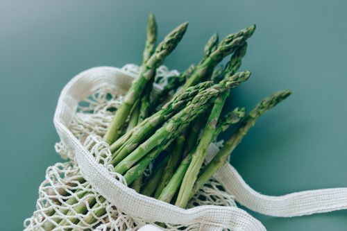 Free Fresh green asparagus in a reusable mesh bag on a green background, showcasing eco-friendly food storage. Stock Photo