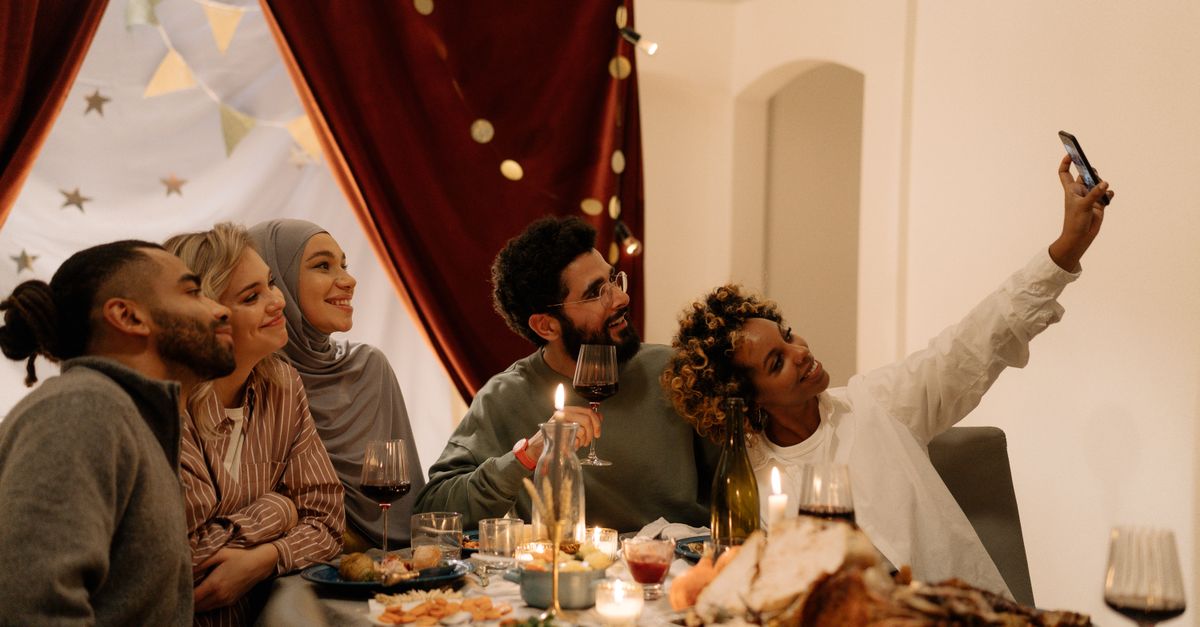 friends laughing at dinner table checking budget app on phone