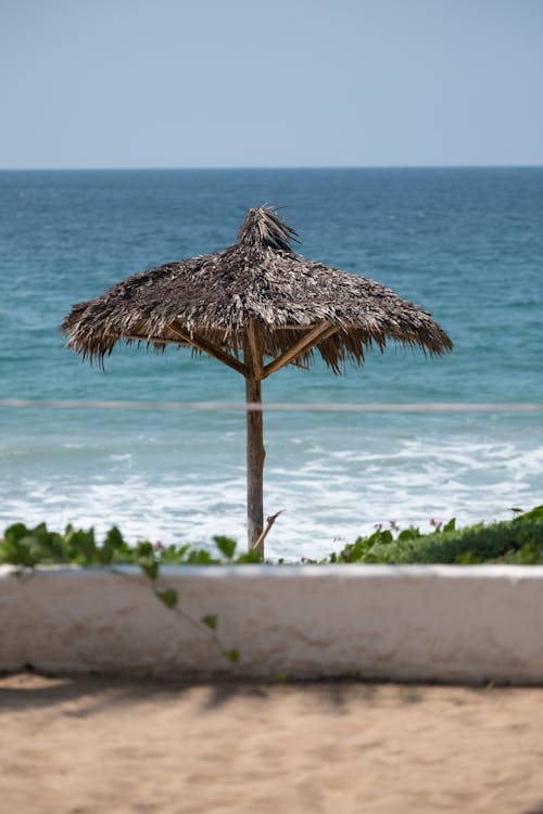 Straw sunshade on coast of tropical azure waving foaming sea at sunlight at resort