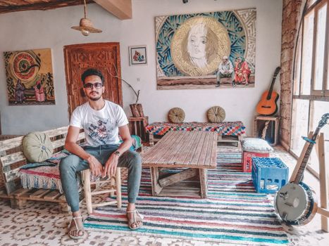Young man sitting in a Moroccan art gallery with musical instruments and vibrant decor.