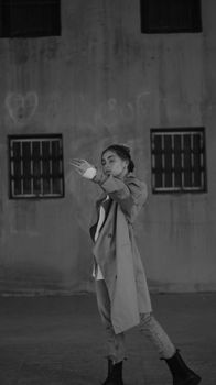 A young woman in a coat stands artistically in a monochrome setting, exuding style.
