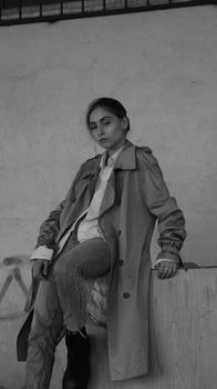 A fashionable woman models a trench coat and jeans in a monochrome indoor setting.