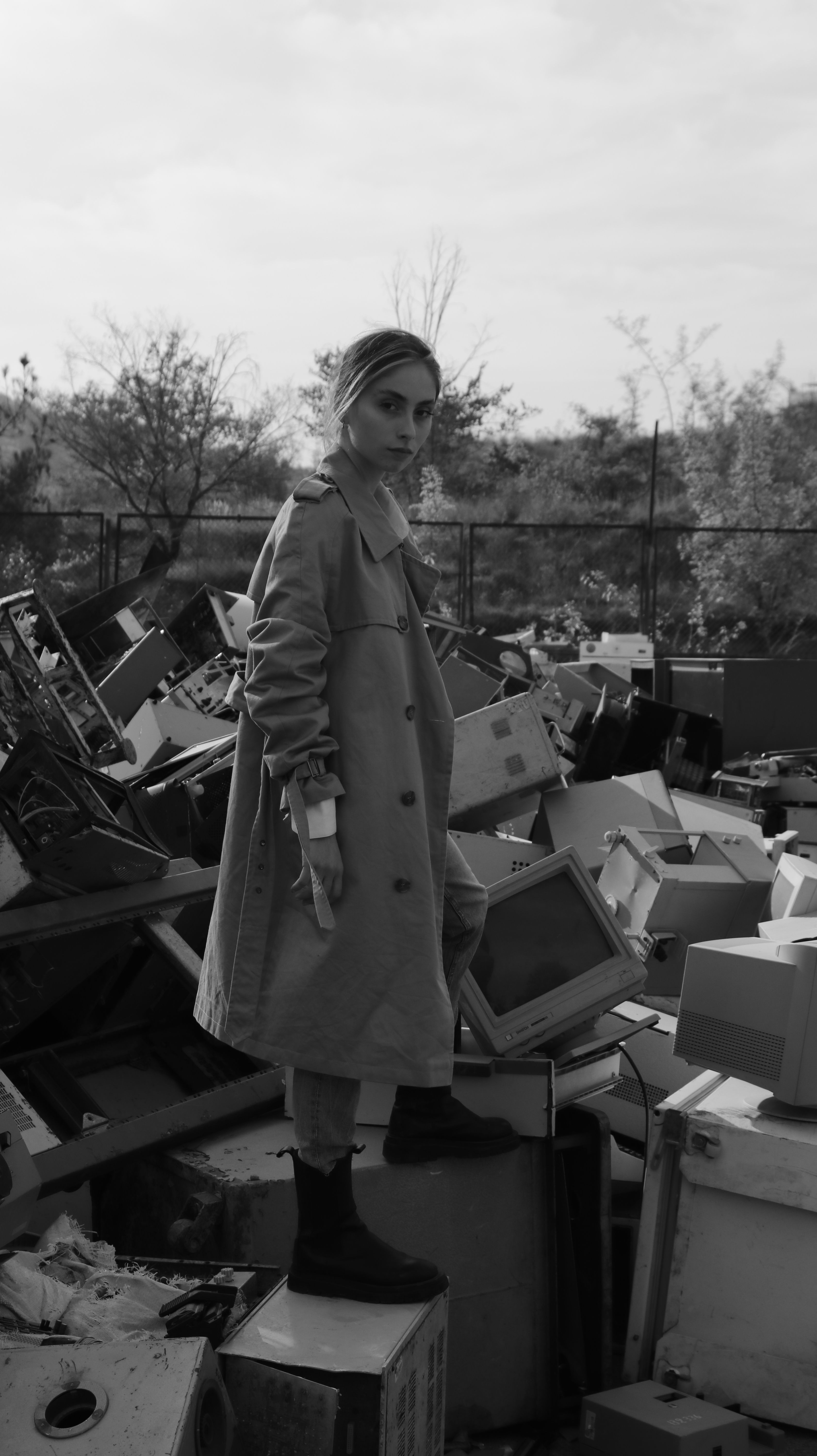 Fashion model in monochrome stands amidst industrial debris showcasing urban style.