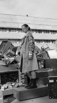 Model posing in a monochrome fashion shoot amidst urban electronic waste.