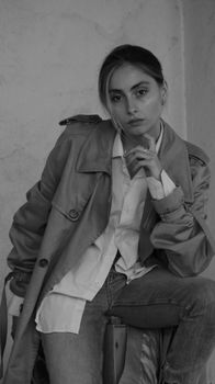Black and white portrait of a stylish woman in a trench coat sitting confidently, enhancing fashion vibes.