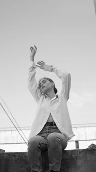 Black and white photo of a woman in a dress shirt, eyes closed, arms raised gracefully.