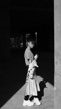 A dramatic black and white portrait of a woman standing in sunlight under a building.