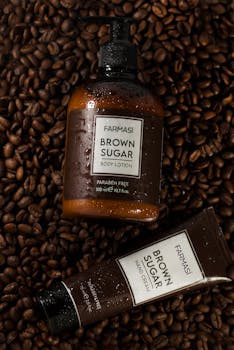 Flat lay of Farmasi brown sugar body lotion and hand cream on coffee beans, showcasing product texture with water droplets.
