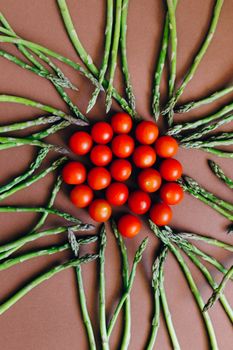 Top view of fresh cherry tomatoes and asparagus creatively arranged on brown background.