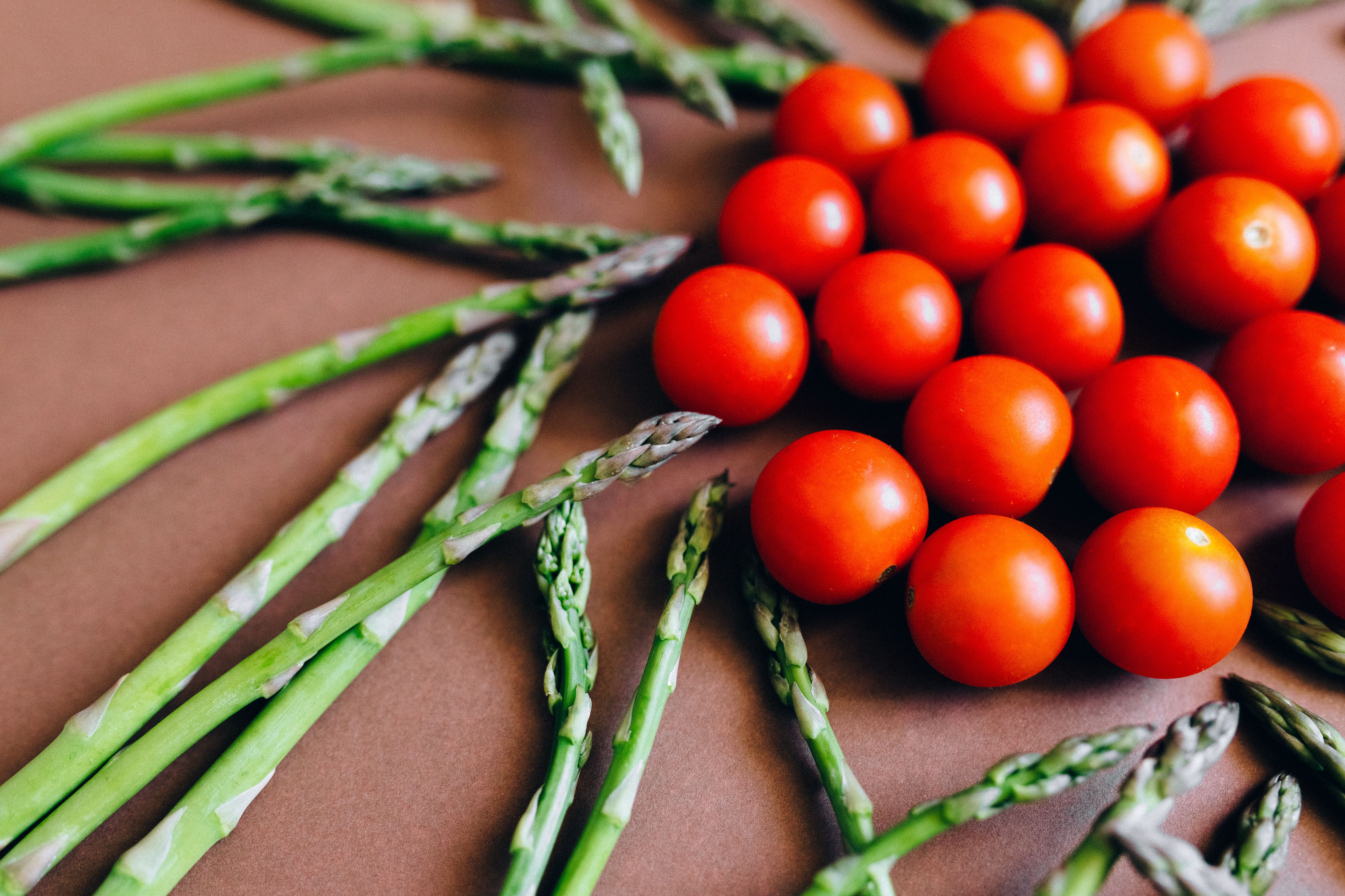 Close-up of fresh asparagus and cherry tomatoes arranged on a brown background.