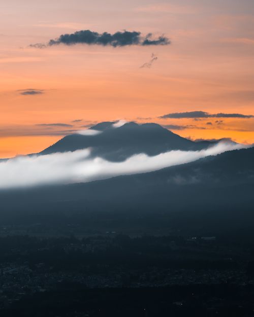 Free A breathtaking sunset over a mist-covered mountain with dramatic clouds. Stock Photo