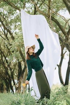 在郁郁葱葱的森林里，一位戴着帽子、穿着绿色毛衣的优雅女人，手里拿着一朵黄色的花