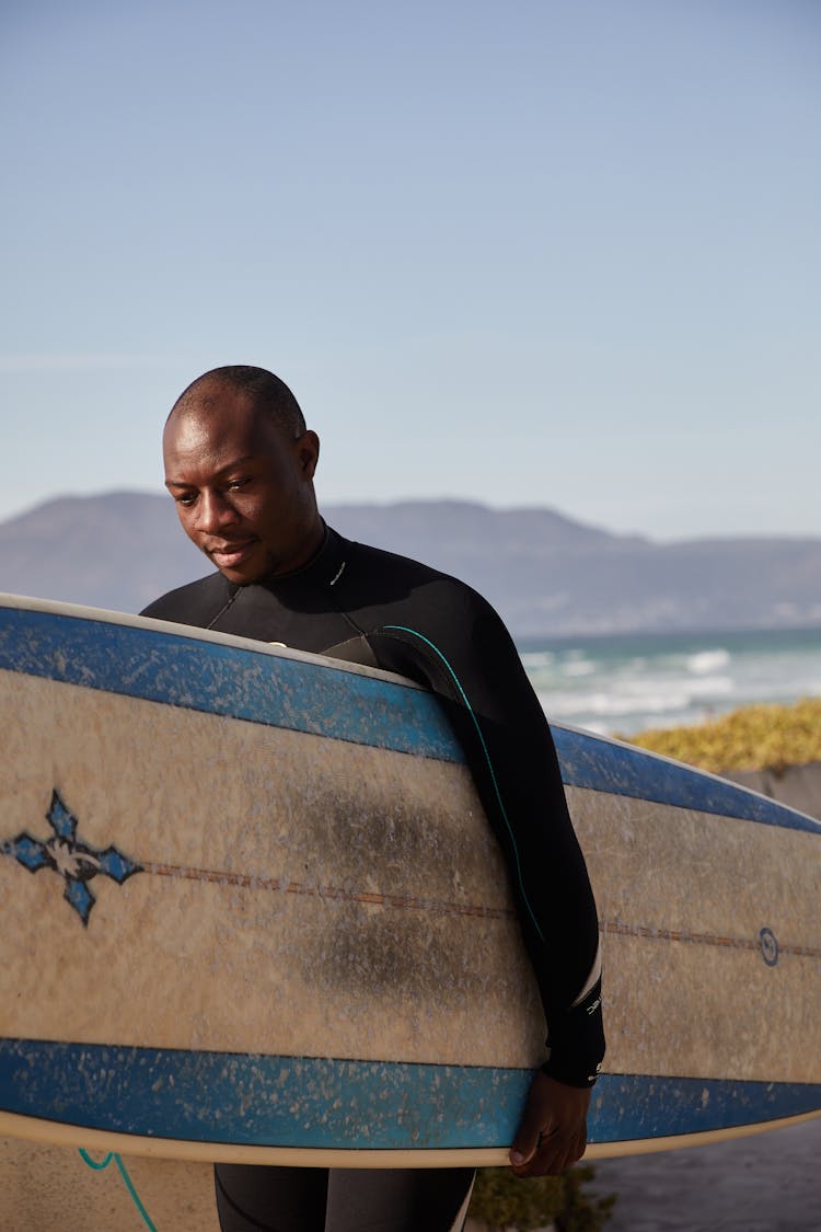 Pondering Black Surfer Carrying Surfboard On Sea Shore