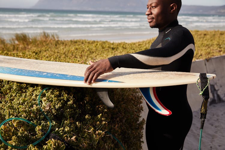 Crop Dreamy Black Surfer With Surfboard Near Bushes On Shore