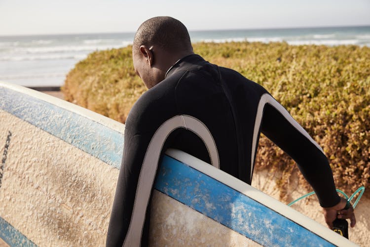 Unrecognizable Black Surfer With Surfboard Near Bushes And Sea