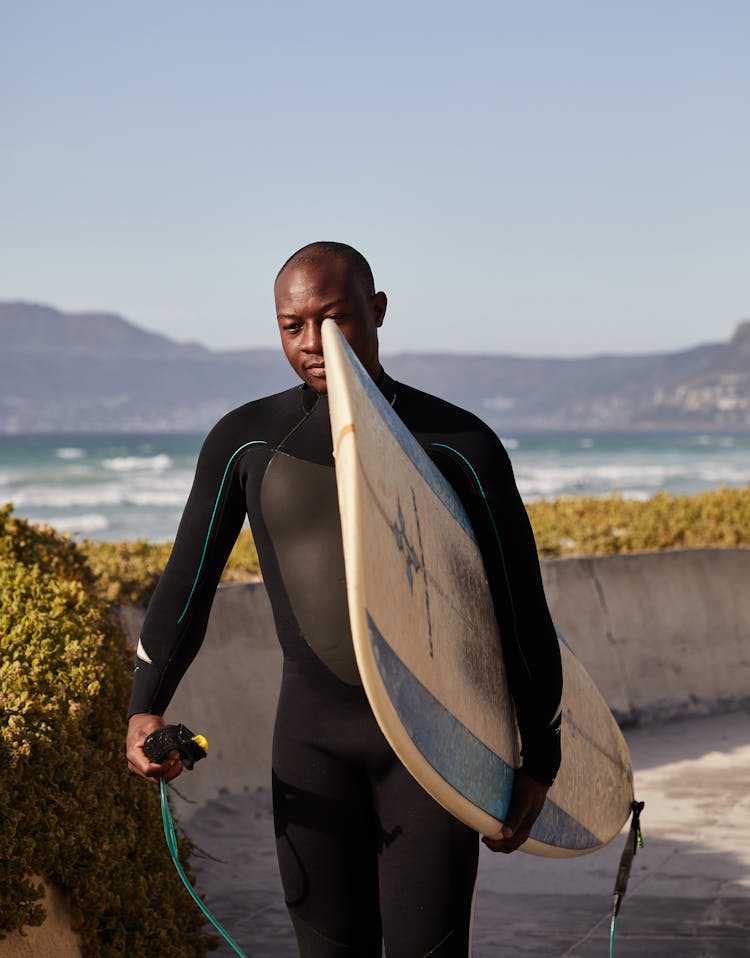 Fit Black Surfer Carrying Surfboard Walking On Embankment