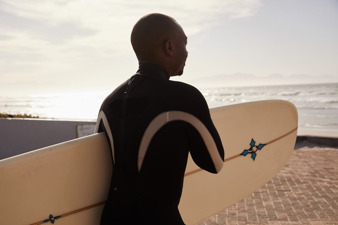 Black man with surfboard on coast of ocean