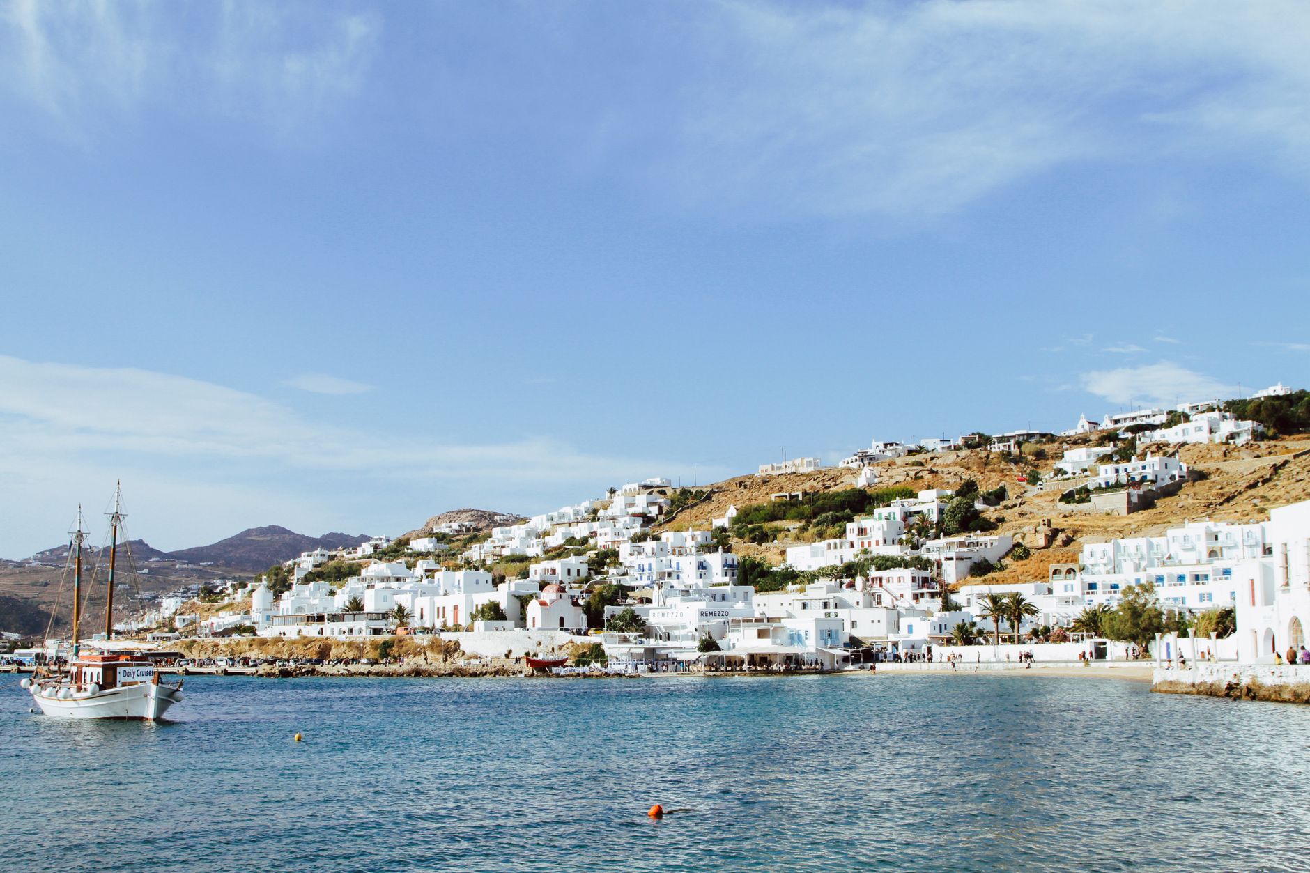 Beautiful view of Mikonos town with traditional architecture and clear blue water harbor.