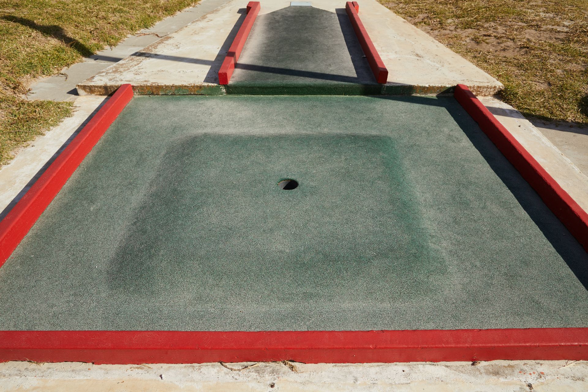 Small round hole in center of square dark green area for mini golf in daytime