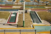 From above of small dark green tracks for mini gold surrounded by multi colored curbs and lawns in sunlight