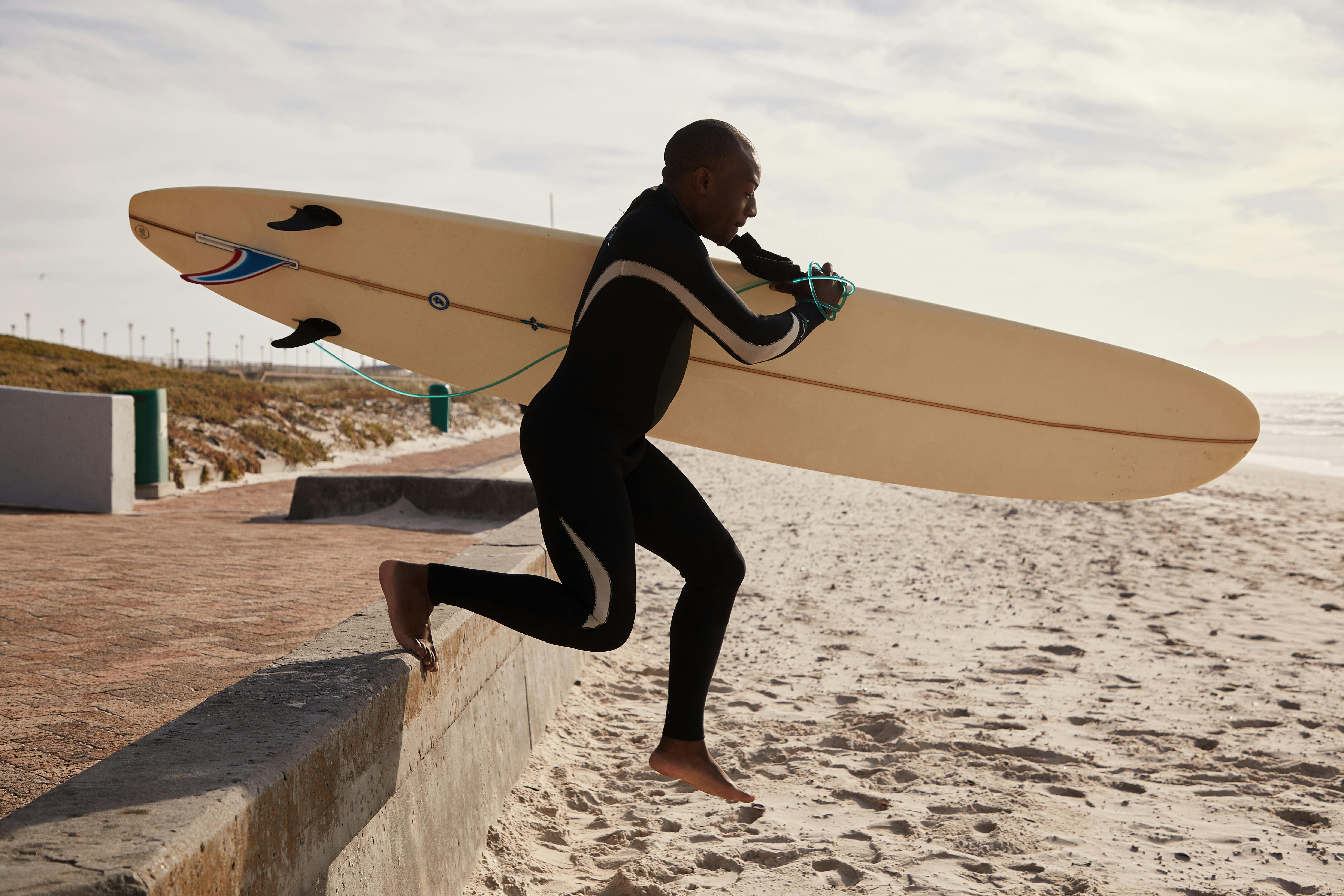 black surfer running to ocean with surfboard in daytime
