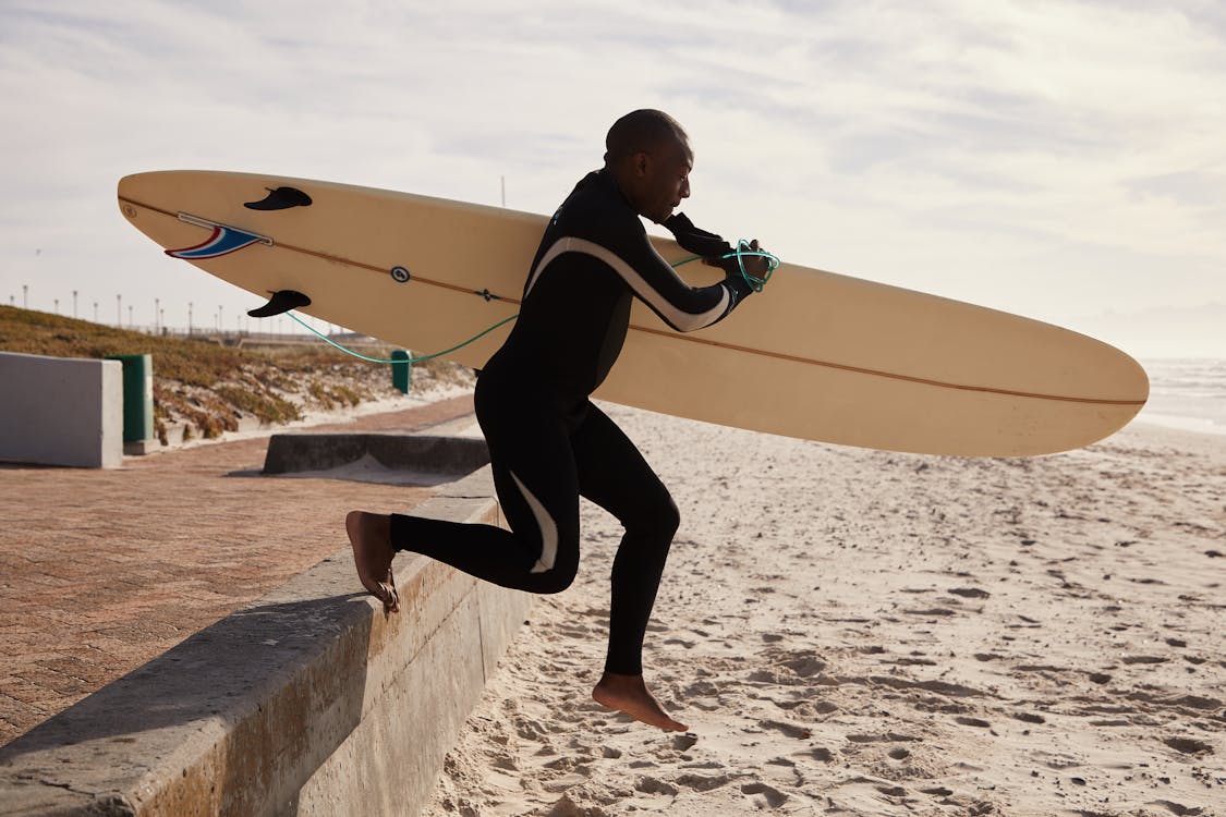 Black surfer running to ocean with surfboard in daytime