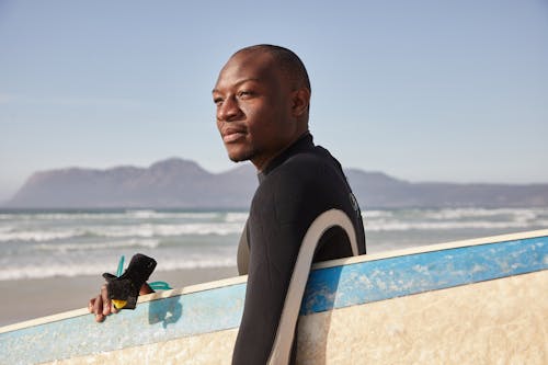 Black man with surfboard on beach