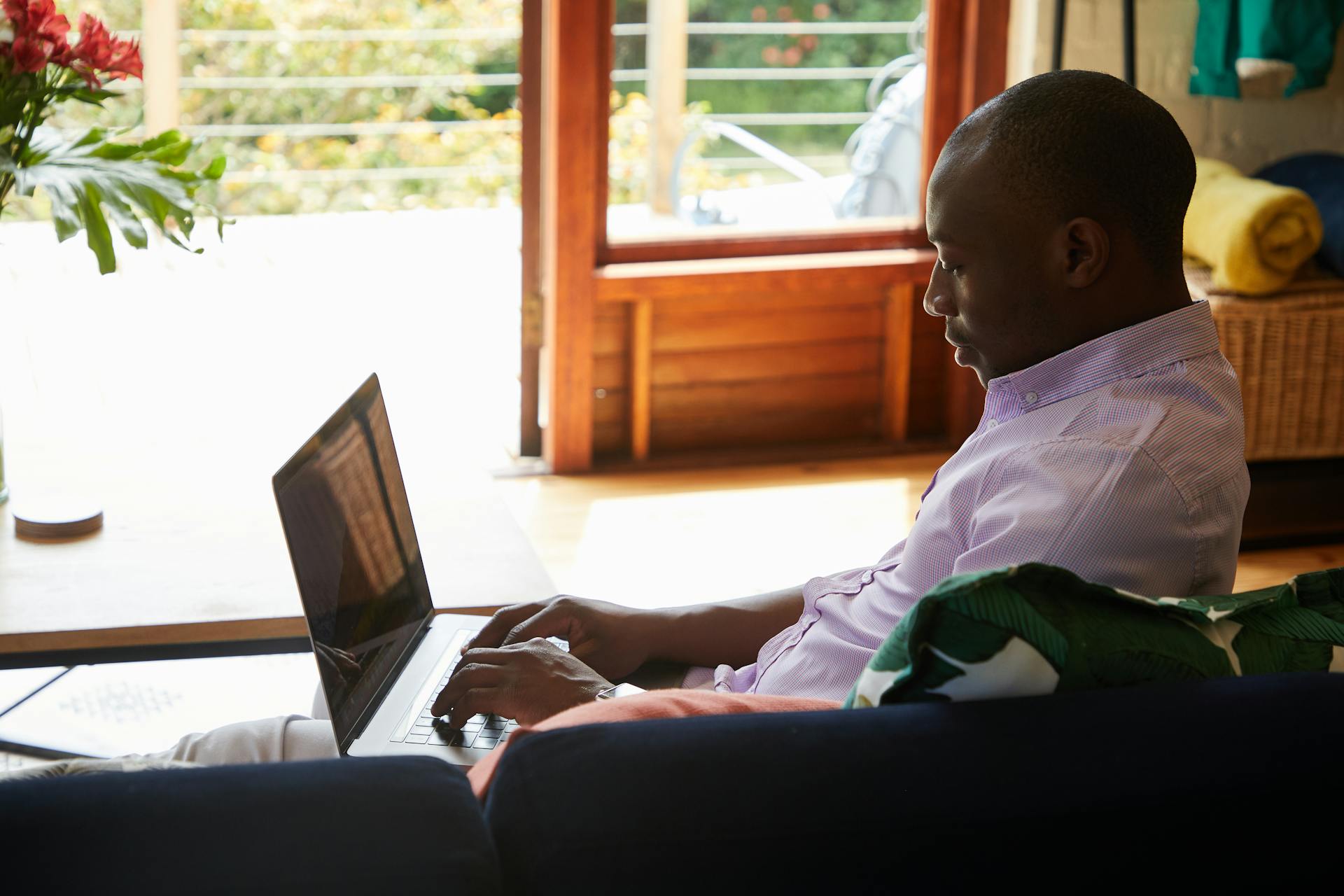 African American man working remotely indoors on a laptop near a window.