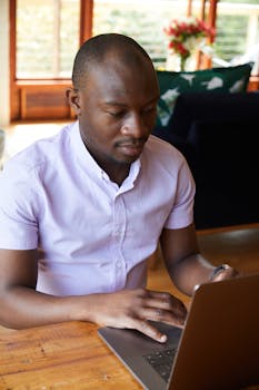 Confident man concentrating on work using a laptop in a well-lit home office.