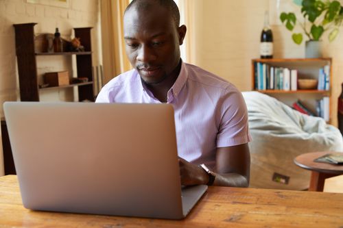 Free Concentrated African American male typing information on netbook at wooden table in cozy living room Stock Photo