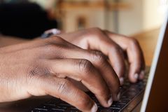 Crop anonymous African American busy male checking email on netbook on blurred background of comfortable room