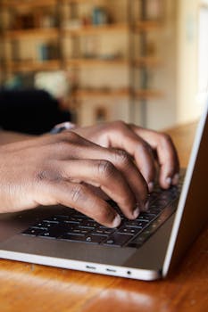 Focused close-up of a person's hands typing on a laptop indoors.