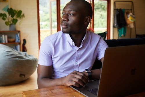 Serious African American male freelancer in formal wear sitting at wooden table while browsing netbook and looking away