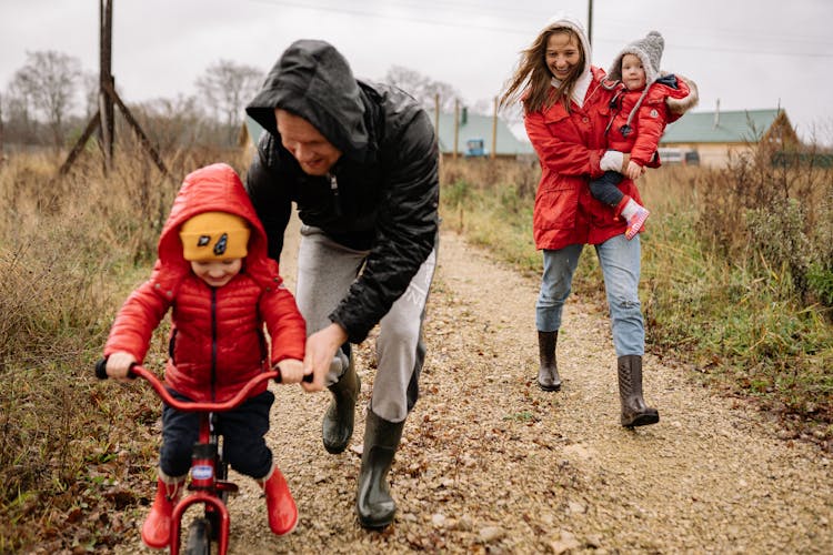 A Woman Carrying Her Baby While Looking At Her Husband Guiding Their Child