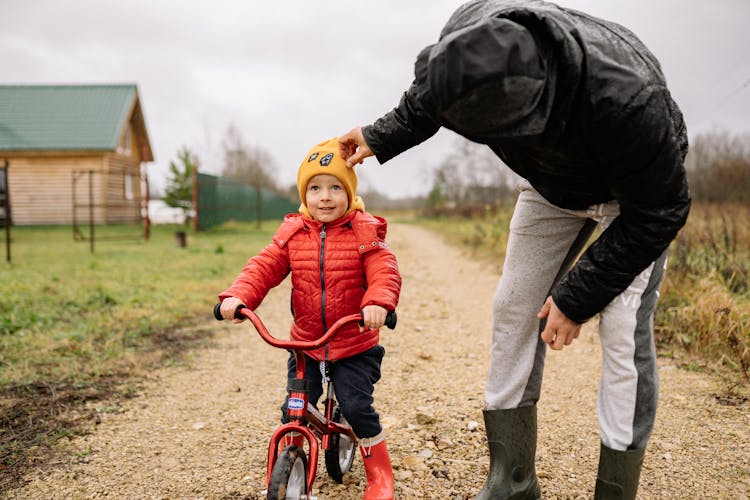 A Child Wearing A Beanie And A Red Jacket Riding A Bike