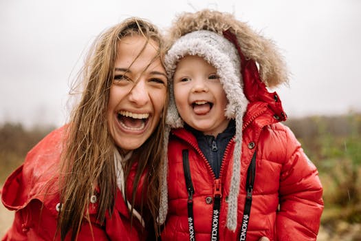 Joyful moment of mother and child laughing in red jackets during rainfall.
