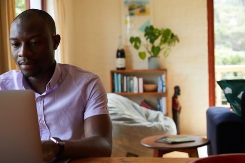 Free Concentrated African American man in formal clothes sitting at table and browsing netbook while working at home Stock Photo