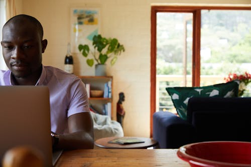 Concentrated African American male freelancer sitting at wooden table and browsing netbook while working online