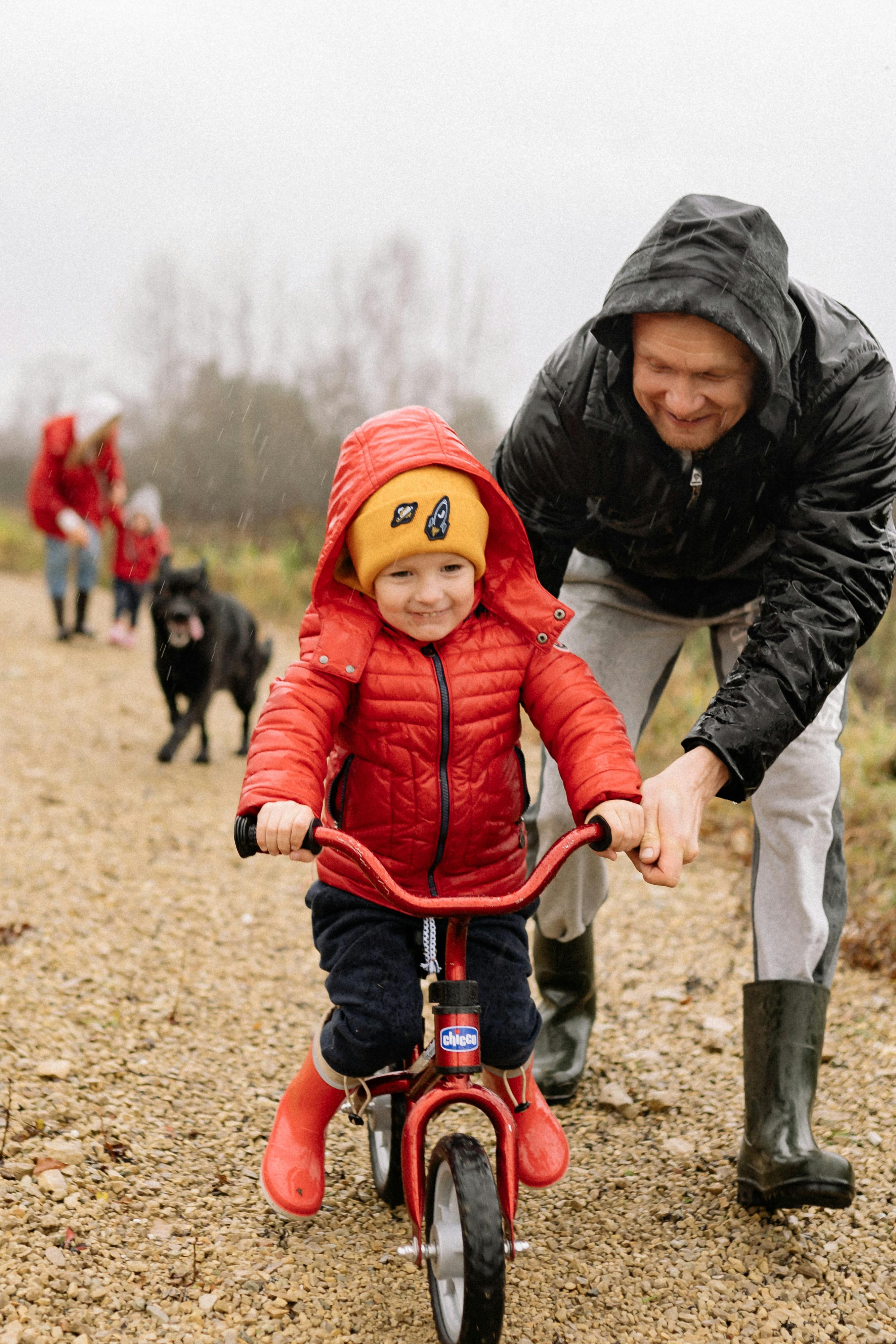Father and child bonding over a bike ride outdoors in rainy weather.