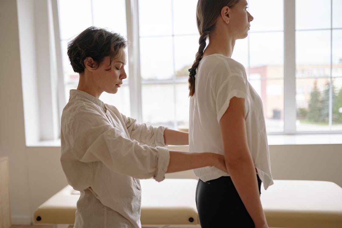 Free A professional therapist adjusting a standing woman indoors. Ideal for healthcare themes. Stock Photo