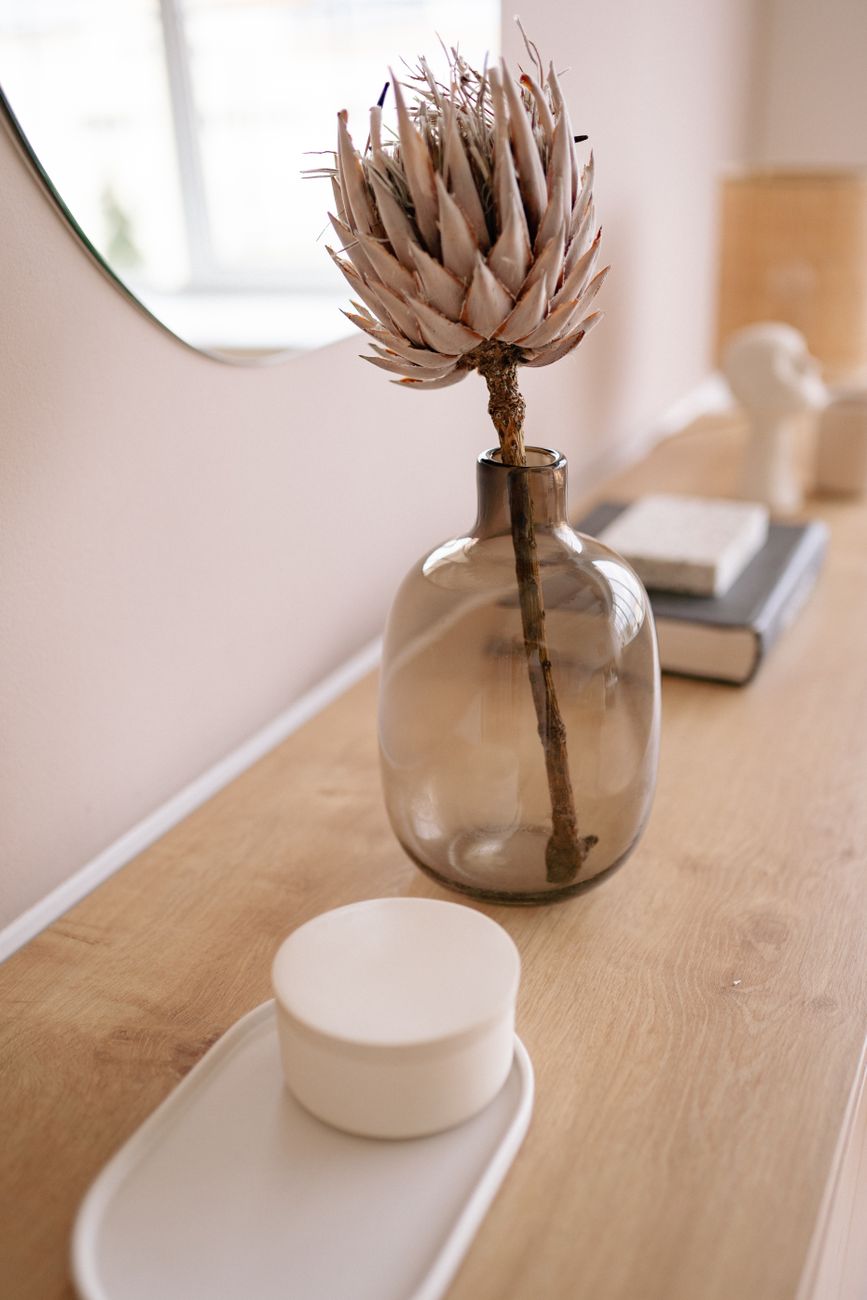 A close-up of a dried protea flower in a glass vase on a wooden table, capturing minimalist decor.