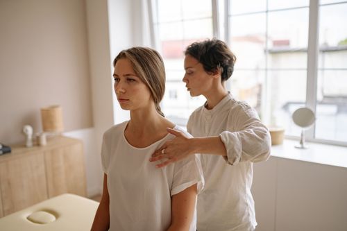 Free A woman receives shoulder therapy from a therapist in a serene room with natural light. Stock Photo