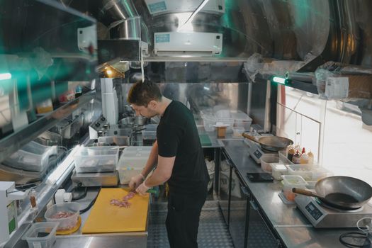 A chef works in a modern industrial kitchen, slicing ingredients on a yellow cutting board.