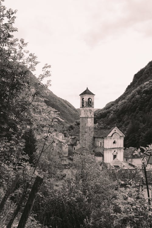 Black and white medieval shabby stone temple located among trees and hills in village