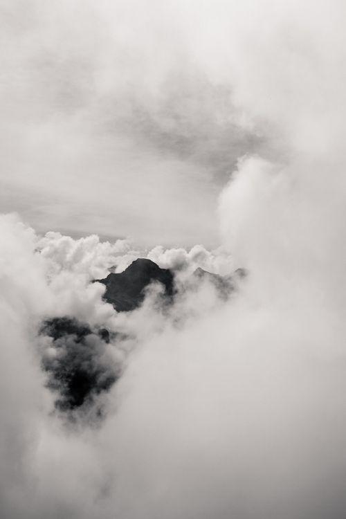 Free Black and white high mountain peak covered with thick fluffy clouds in overcast day Stock Photo